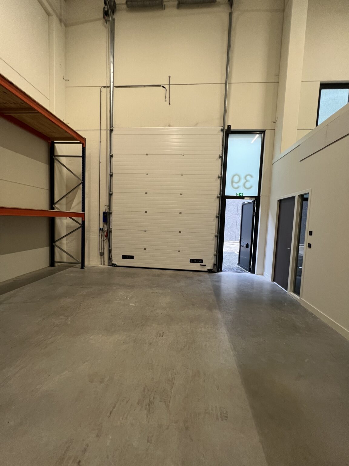 Een lege opslagruimte met een betonnen vloer, hoge plafond en een grote garagedeur, genummerd 33.